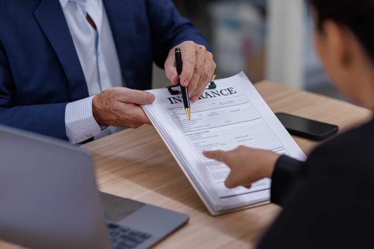 Senior couple reviewing insurance papers and a medication list at a kitchen table.